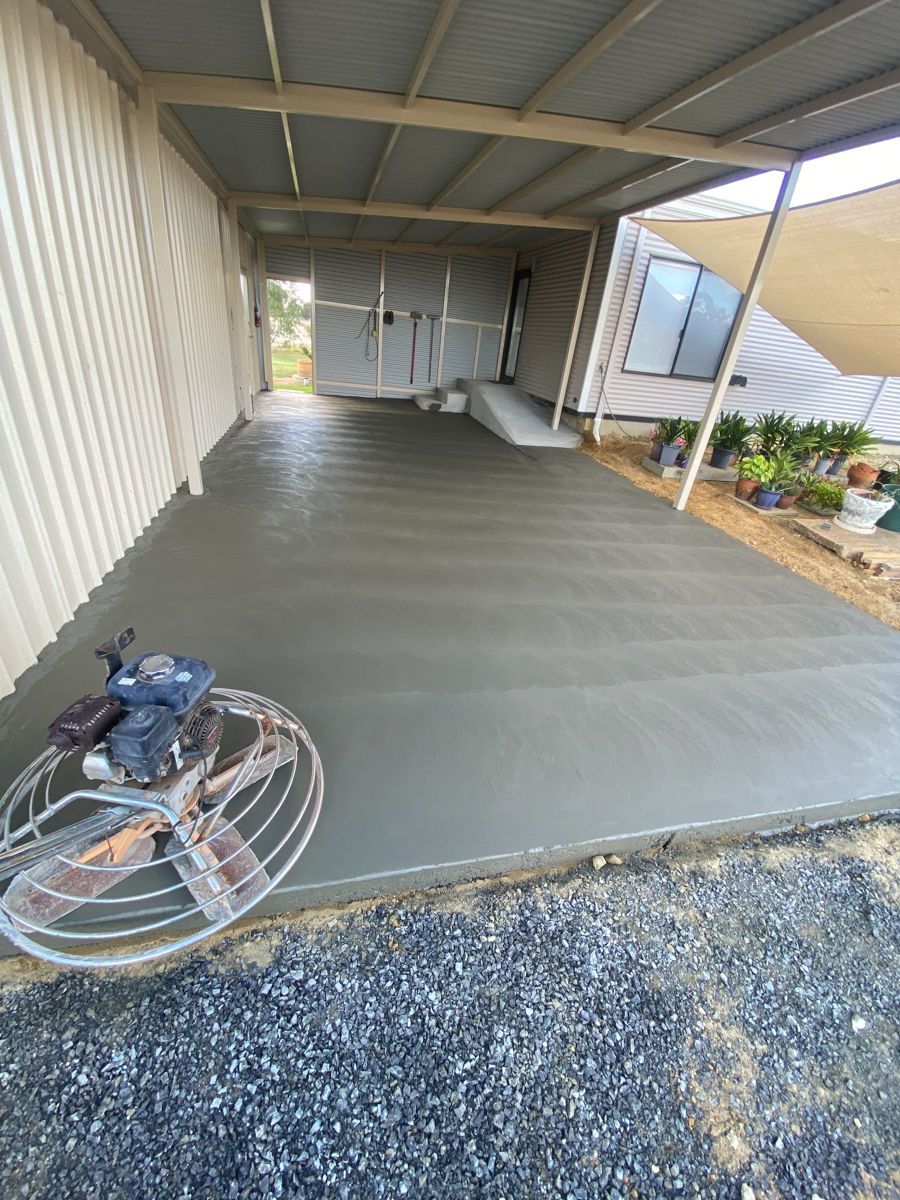 Construction worker on concrete slab, wearing a hard hat and neon vest, bending to work with tools.