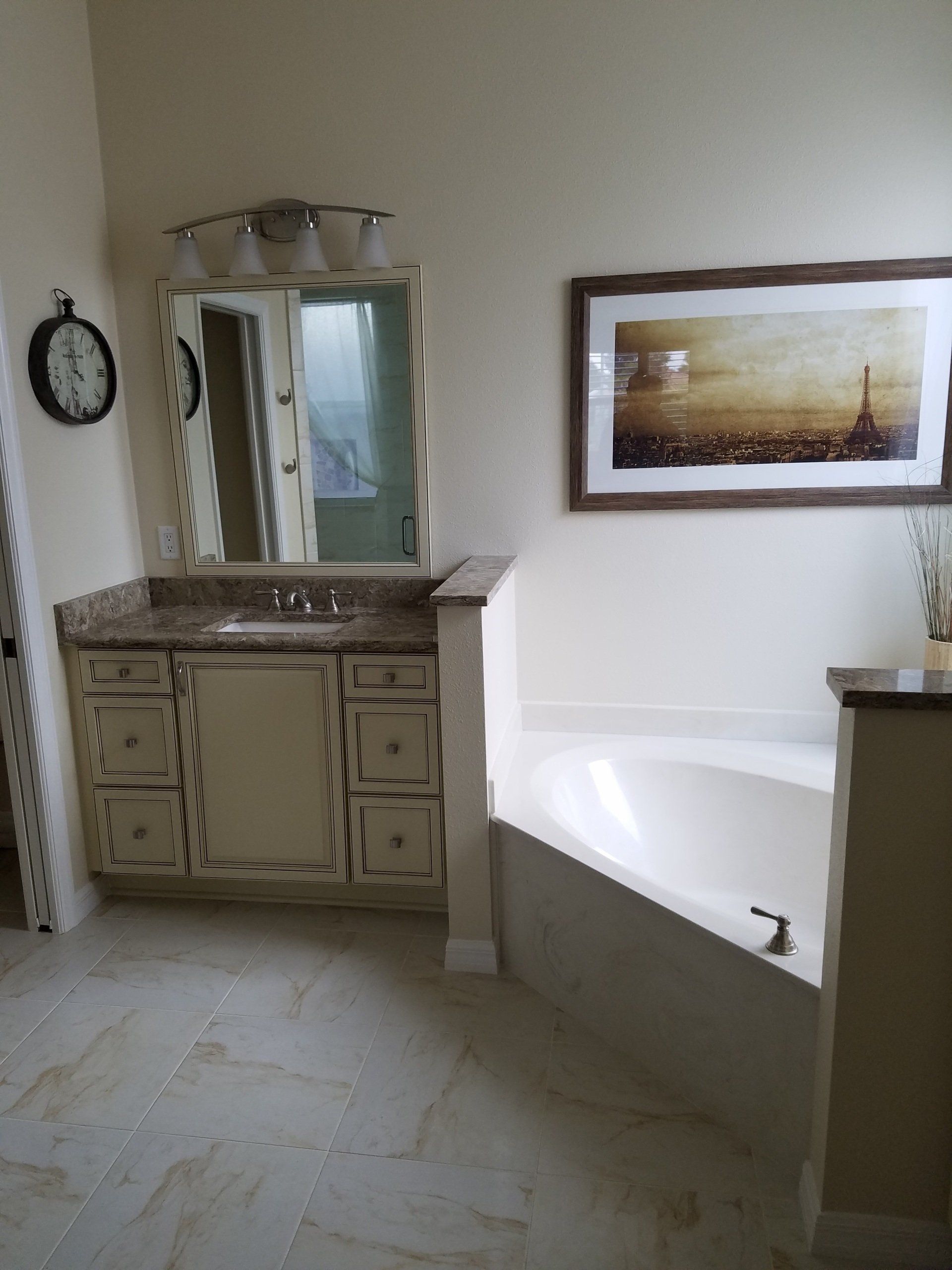 Bathroom with vanity, tub, and framed artwork. Beige walls and floor, brown countertops.