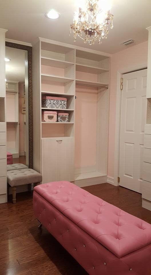 Pink walk-in closet with built-in shelving, a bench, a large mirror, and a chandelier.