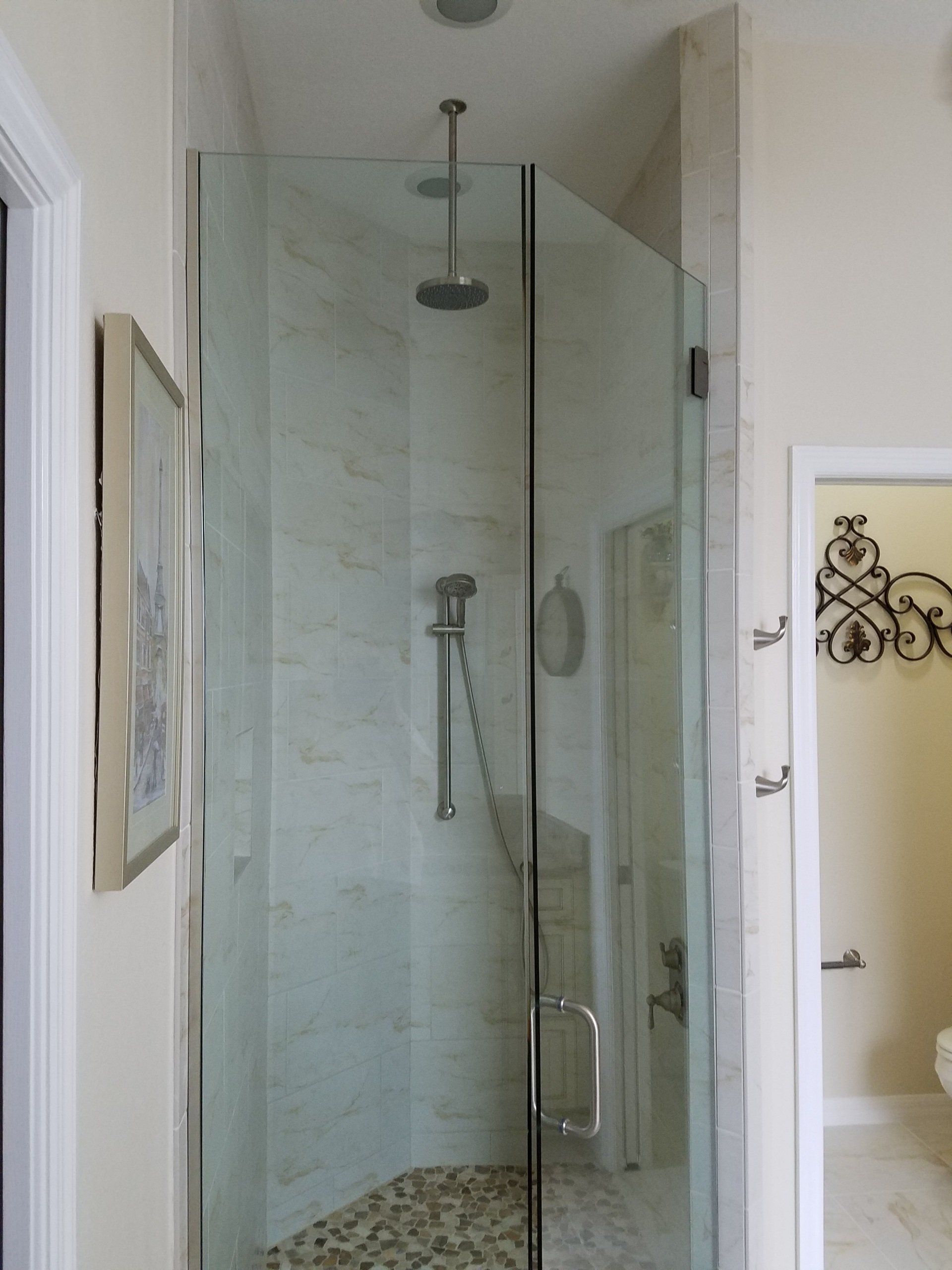 A glass shower enclosure with a rain shower head, pebble floor, and marble tiles.