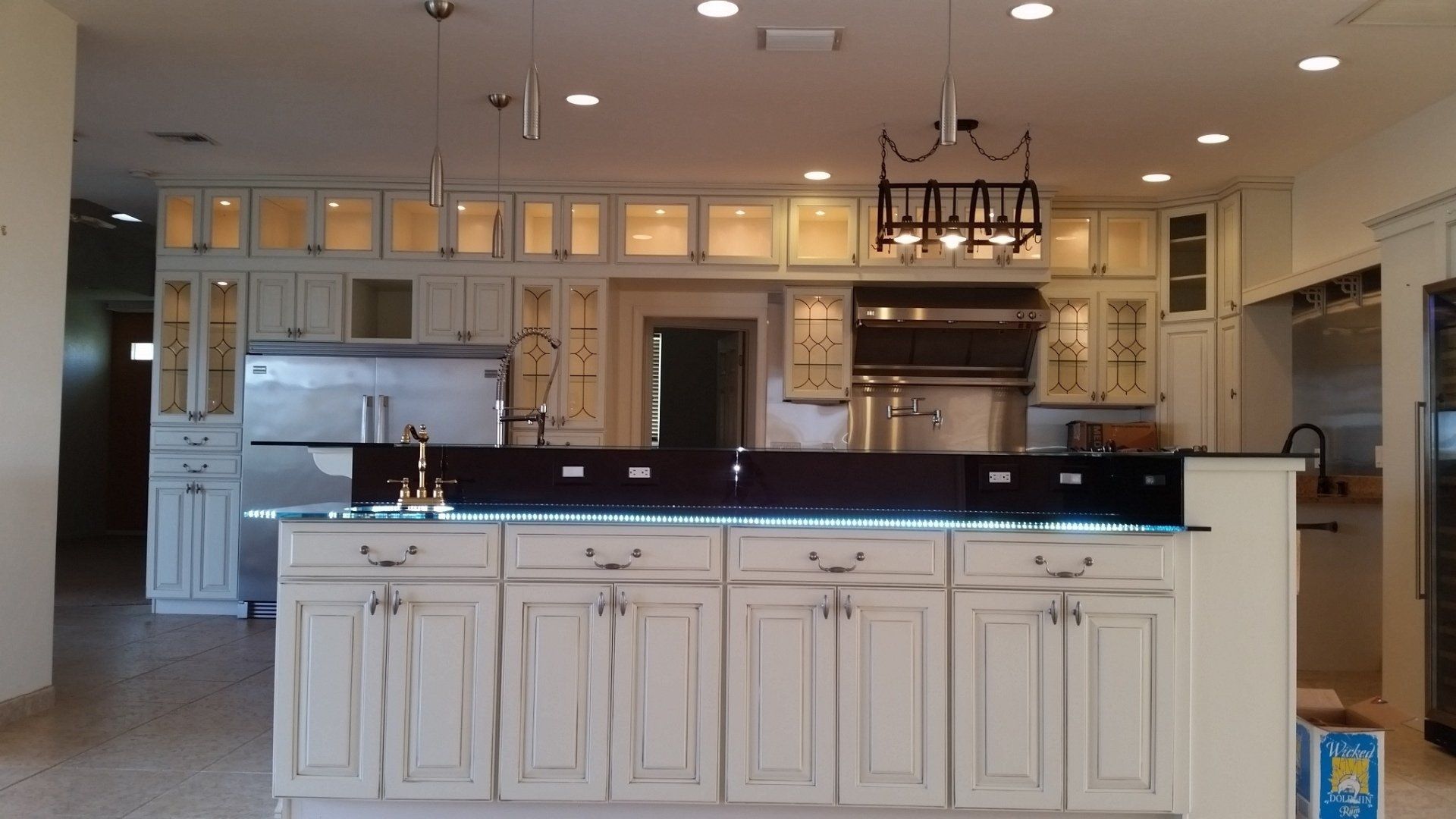 Spacious white kitchen with central island, upper cabinets, stainless steel appliances, and black countertop accents.