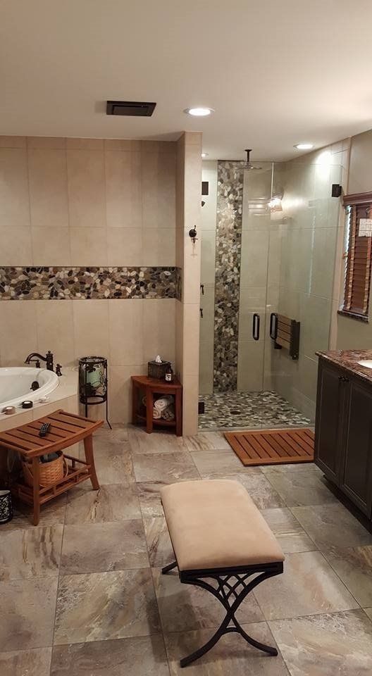 Spa-like bathroom with stone tile, glass shower, jacuzzi, wood accents, and a bench.