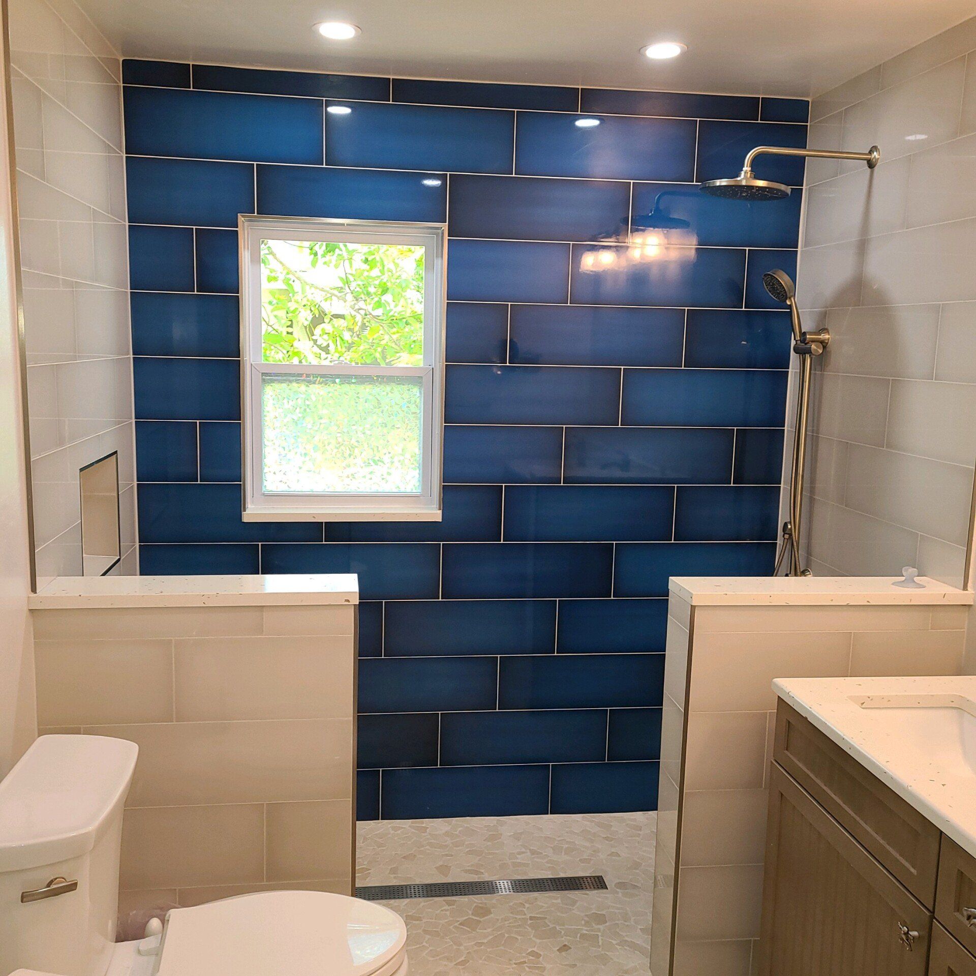 Bathroom with blue tile shower wall, a window, and a toilet.