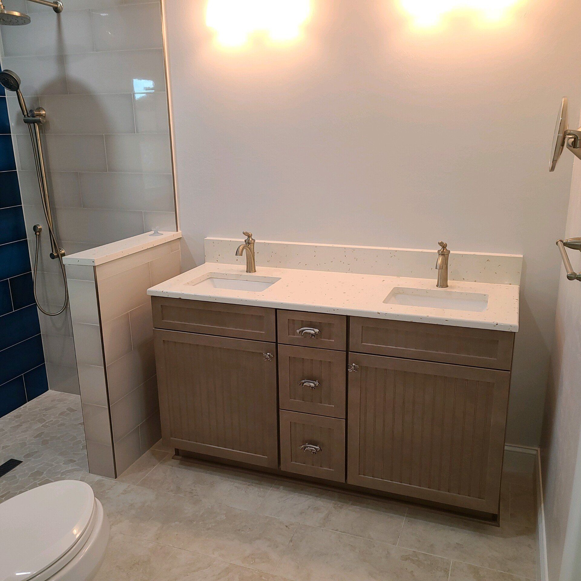 Bathroom with double vanity, gold fixtures, beige cabinets, white countertop, and a shower.