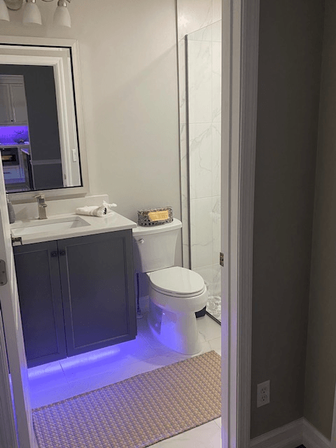 Bathroom with a gray vanity, white toilet, and purple under-cabinet lighting.