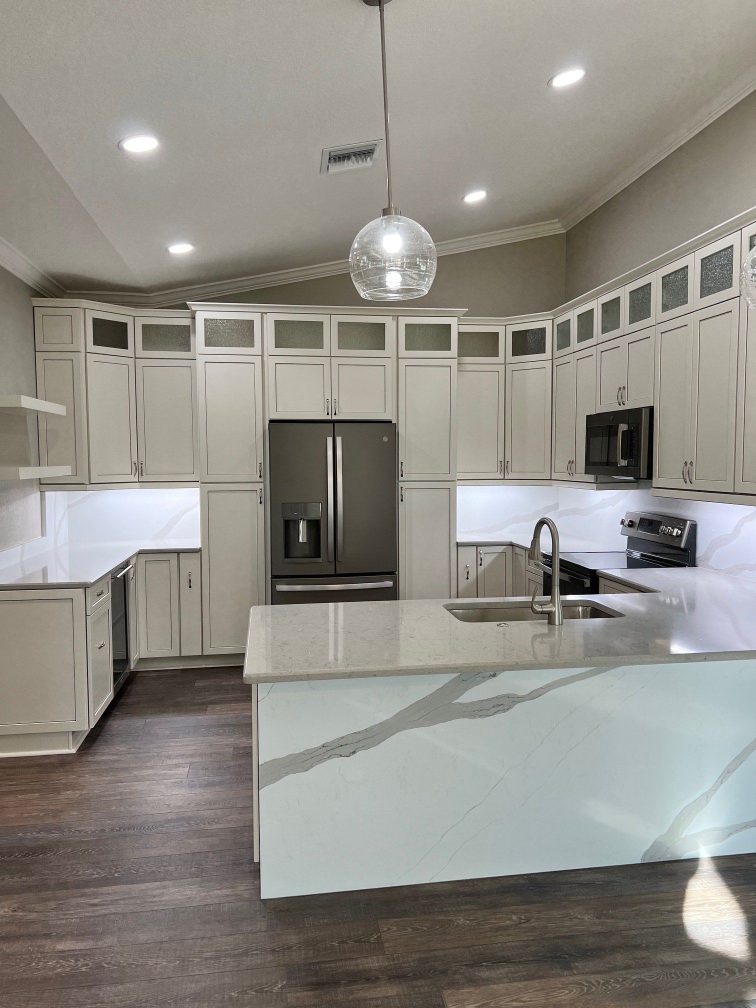 Modern kitchen with light gray cabinets, white countertops, stainless steel appliances, and an island.