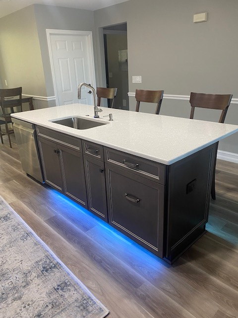 Kitchen island with a sink, cabinetry, and blue under-cabinet lighting; three chairs face the island.