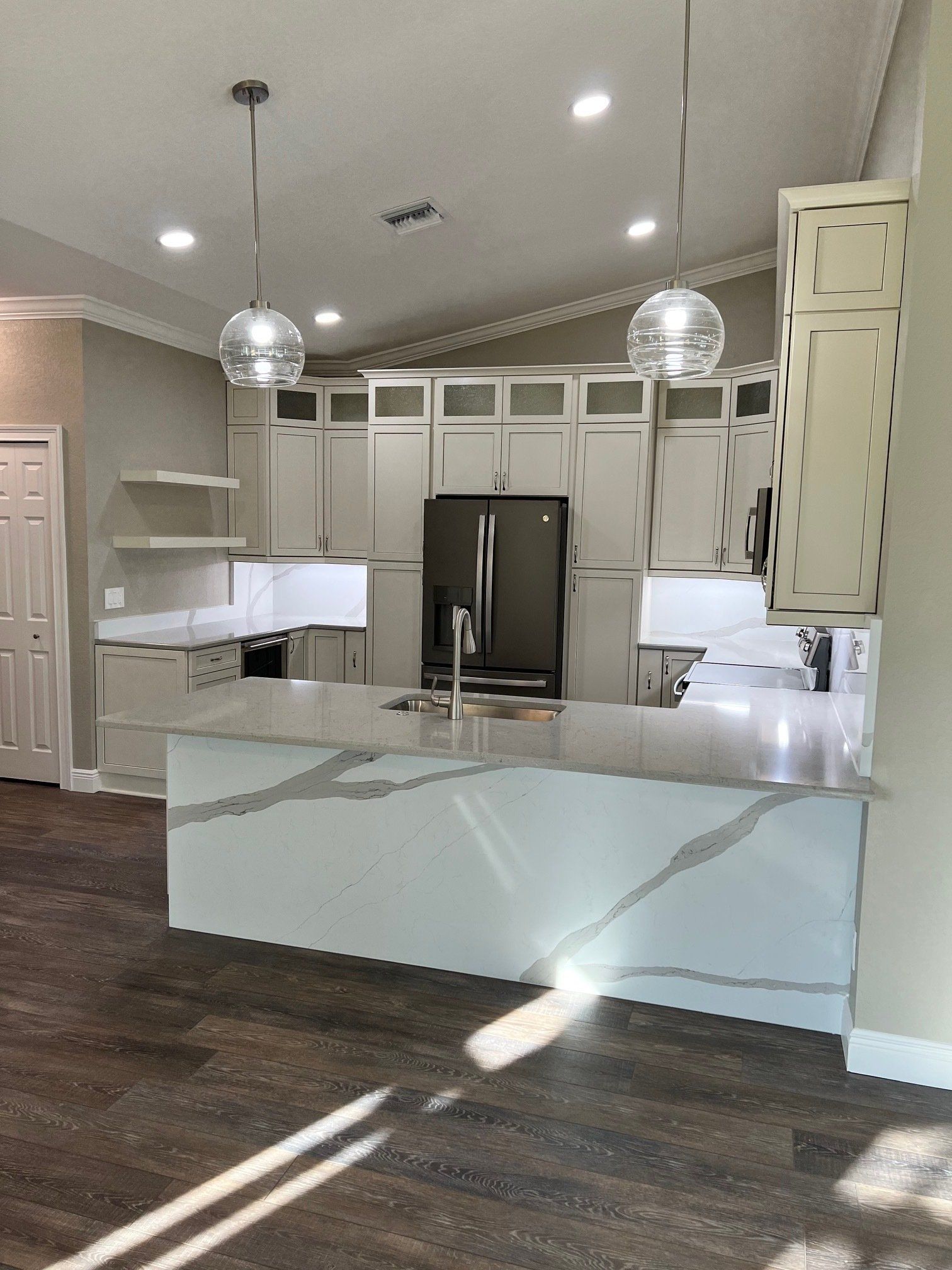 Modern kitchen with a large island and gray cabinets; pendant lights hang above.