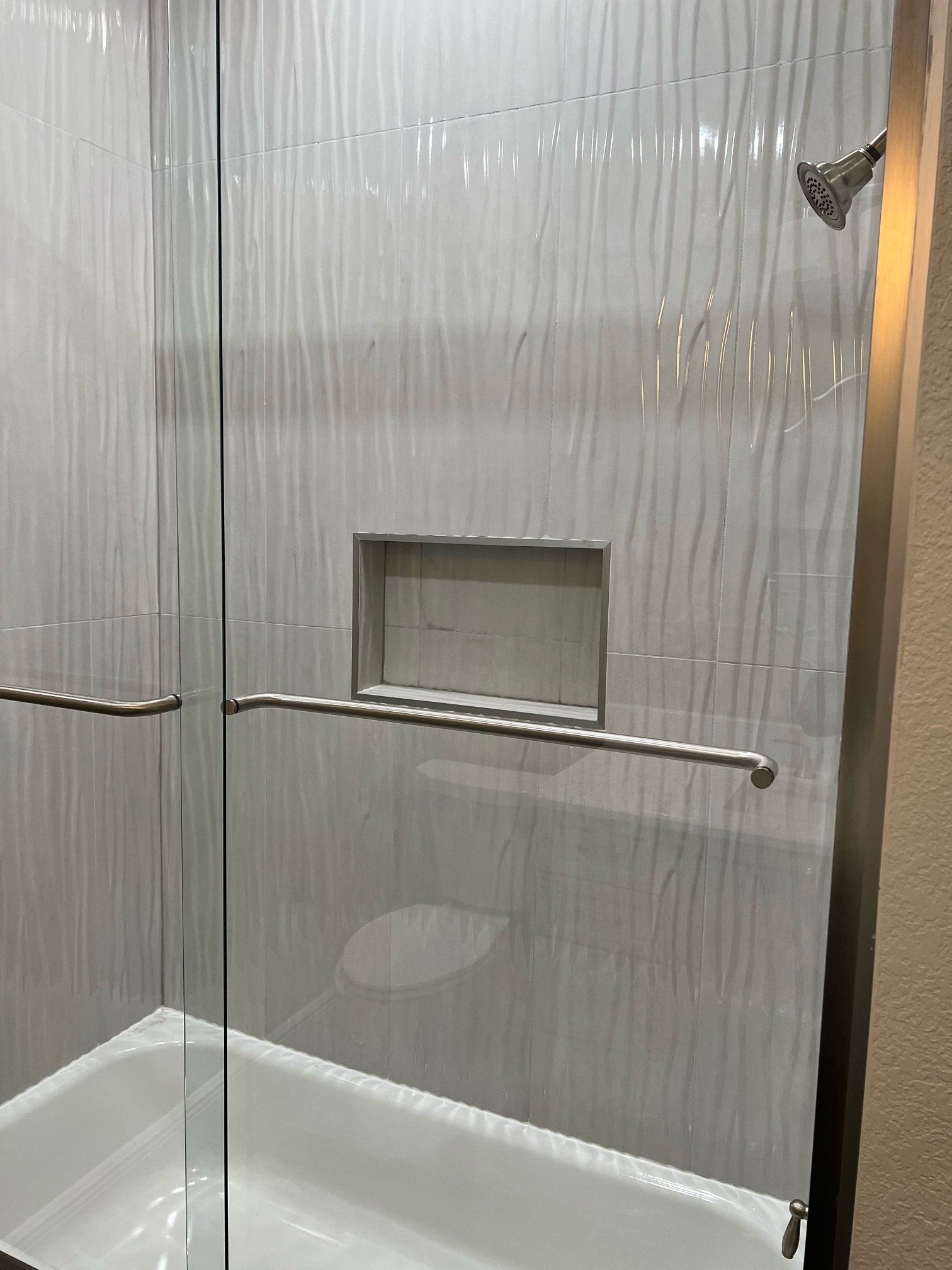 White tiled shower with a glass door and built-in shelf.