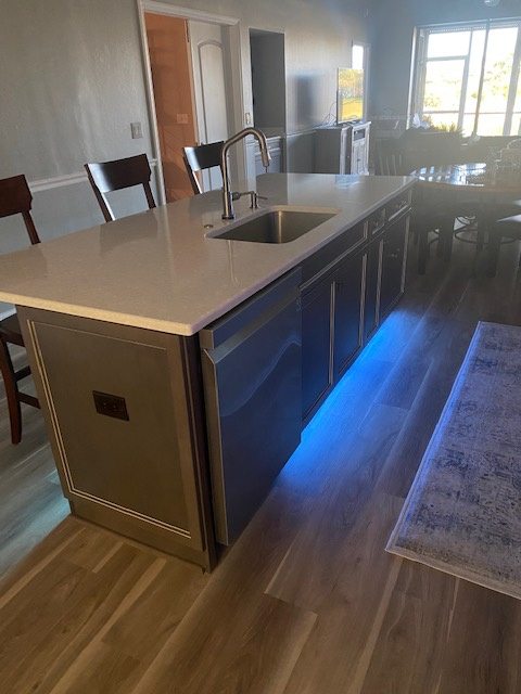 Kitchen island with blue under-cabinet lights, a sink, and dark cabinets in a well-lit room.