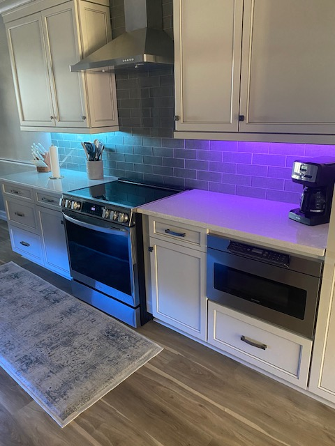 Kitchen with white cabinets, stainless steel appliances, and colorful under-cabinet lighting.