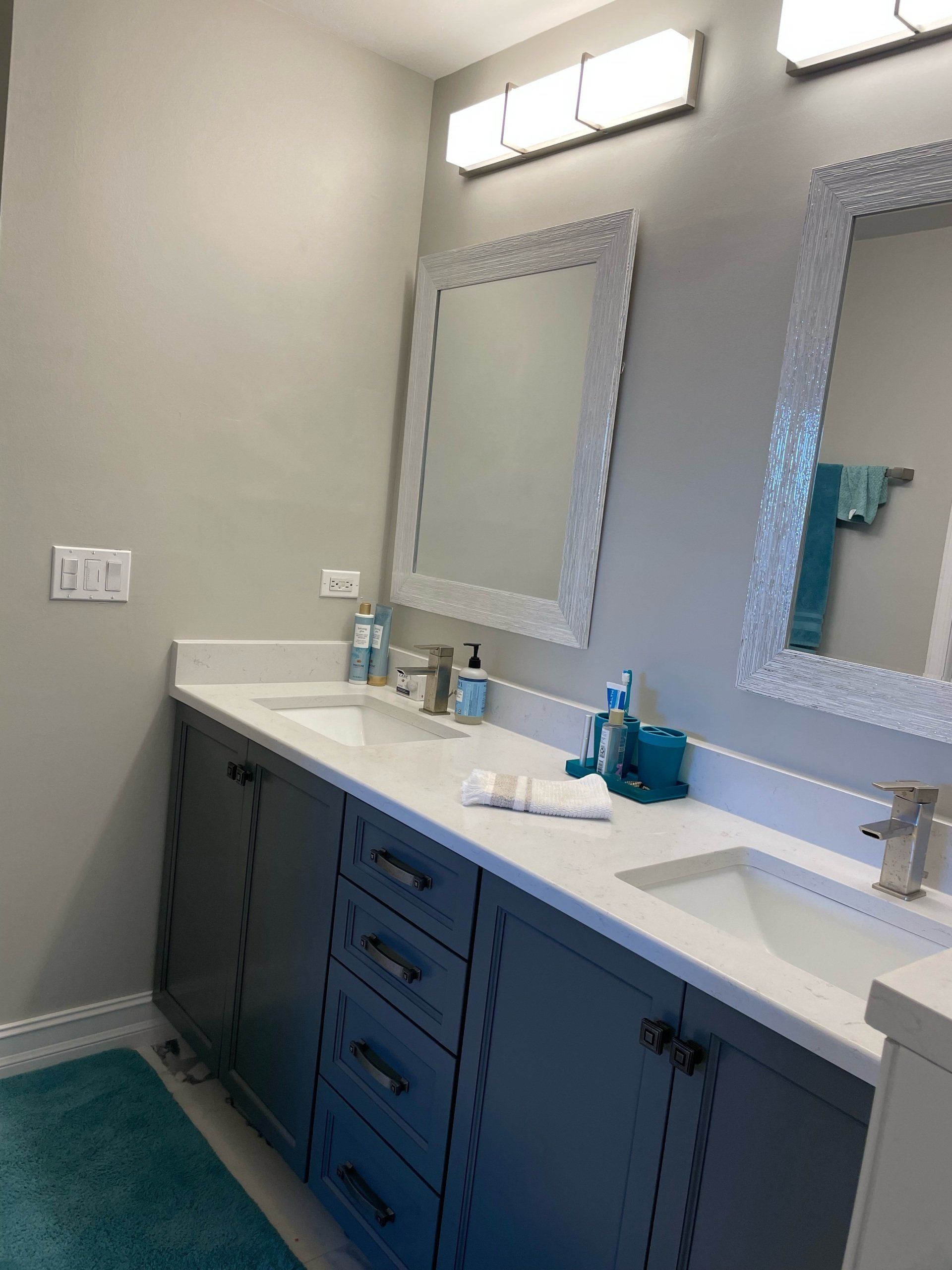 Bathroom with gray cabinets, white countertops, and crystal-framed mirrors. Teal accents.