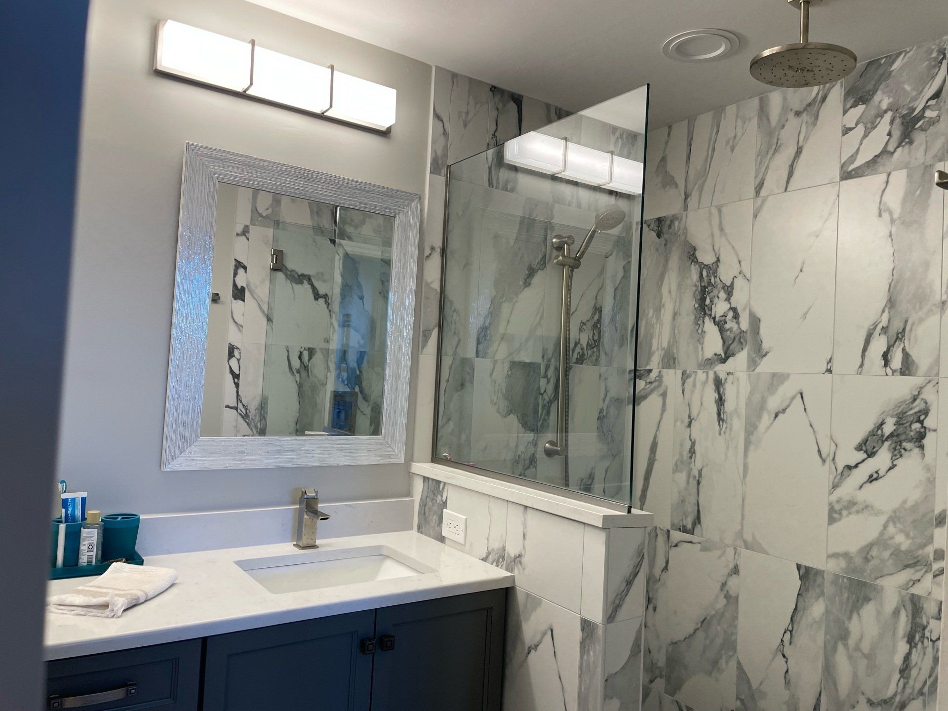 Bathroom with gray vanity, marble-look tile, glass shower, and a framed mirror.
