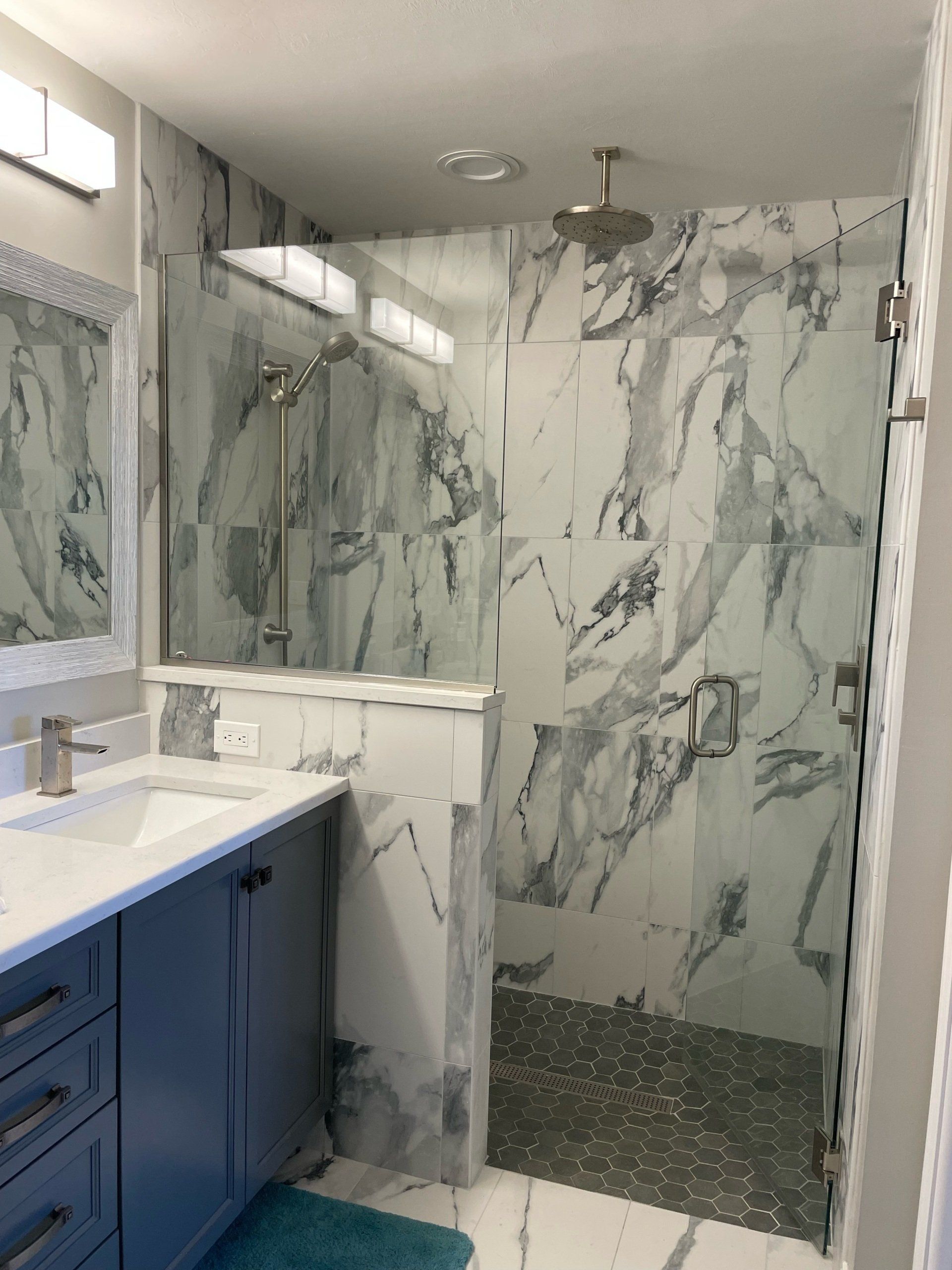 Bathroom with marble-look tile, glass shower door, blue vanity, and silver fixtures.