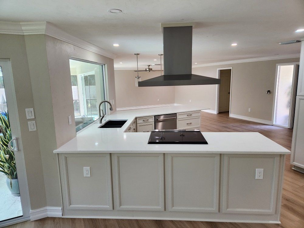 Modern kitchen with white cabinetry, island, stainless steel hood, and hardwood floors.