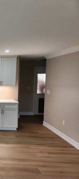 Interior view of a kitchen with light cabinets, wood floors, and a hallway.