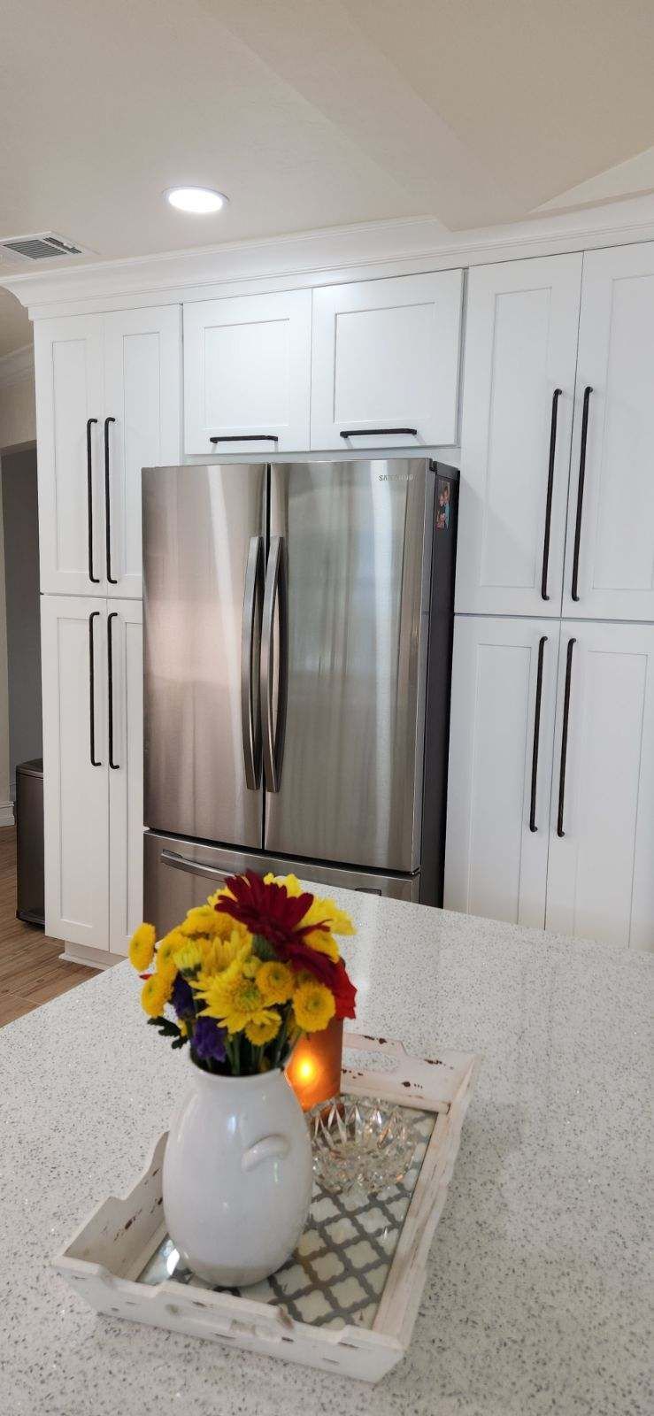 White kitchen with a stainless steel refrigerator, countertop with flowers.