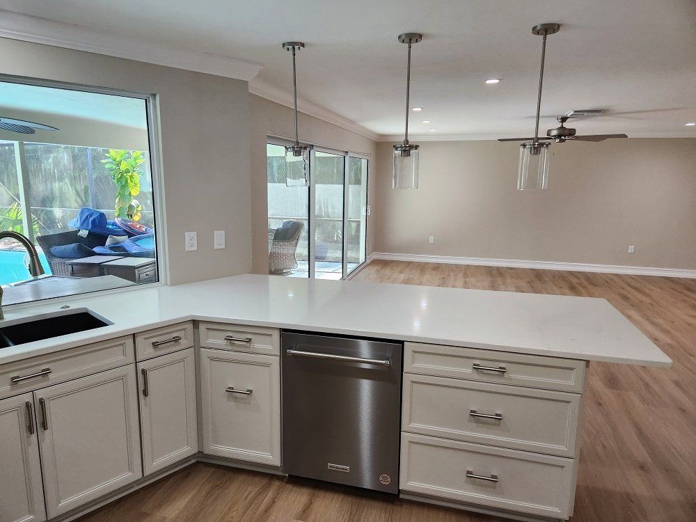 Kitchen with white cabinets, island, stainless steel dishwasher, and hanging lights; sliding glass doors to patio.