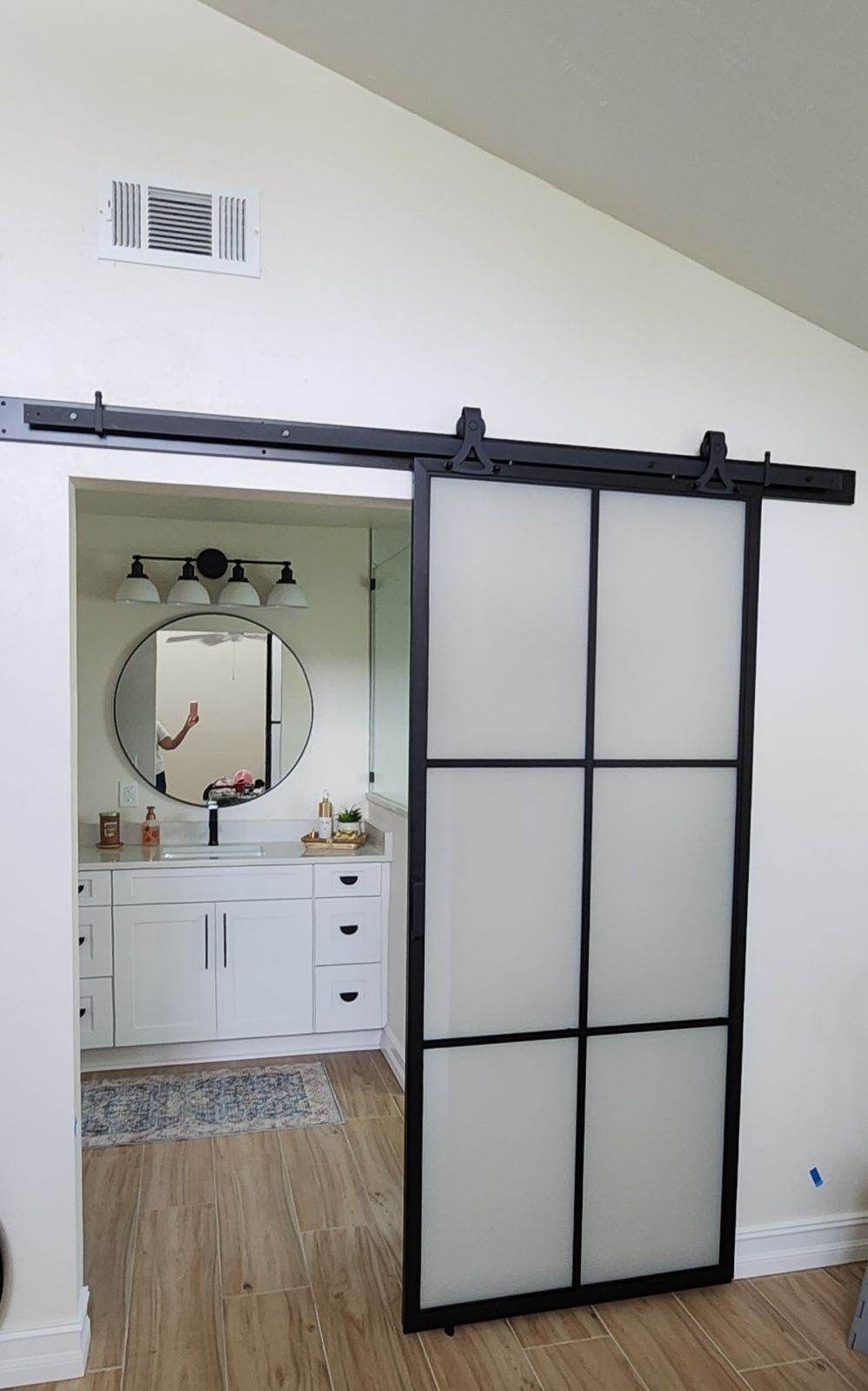 Black framed frosted glass barn door leading to a white bathroom with a circular mirror and vanity.