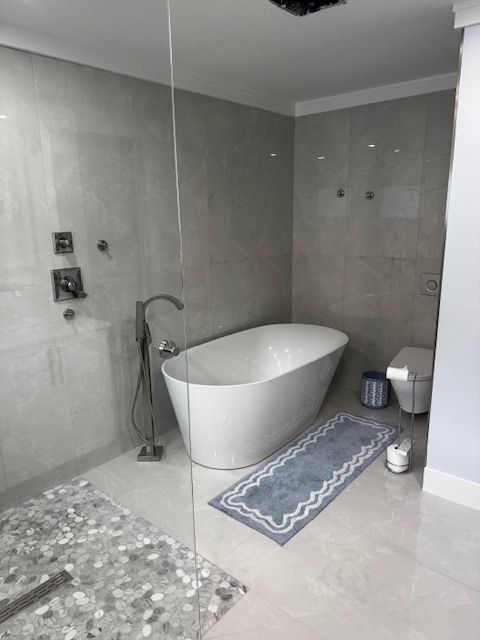 Bathroom with white vanity, toilet, marble-tiled shower, and framed mirror. Wooden floor and blue-gray wall.