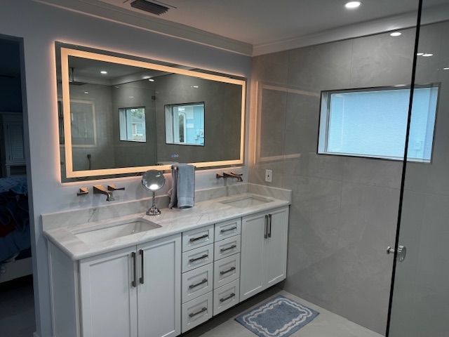Bathroom with white vanity, toilet, and shower, featuring wood-look flooring and marble-patterned wall tiles.