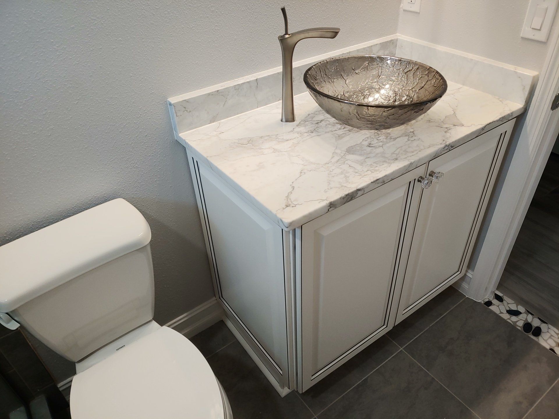 Bathroom vanity with a vessel sink, countertop, and white cabinets. Toilet to the left.
