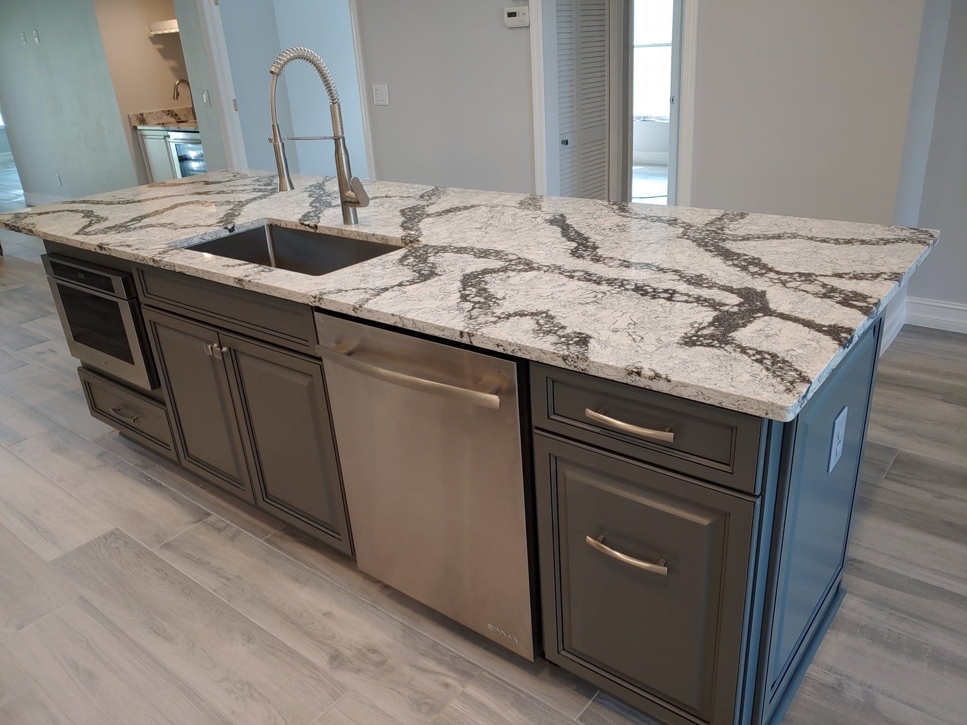 Gray kitchen island with marble countertop, sink, dishwasher, and cabinetry.