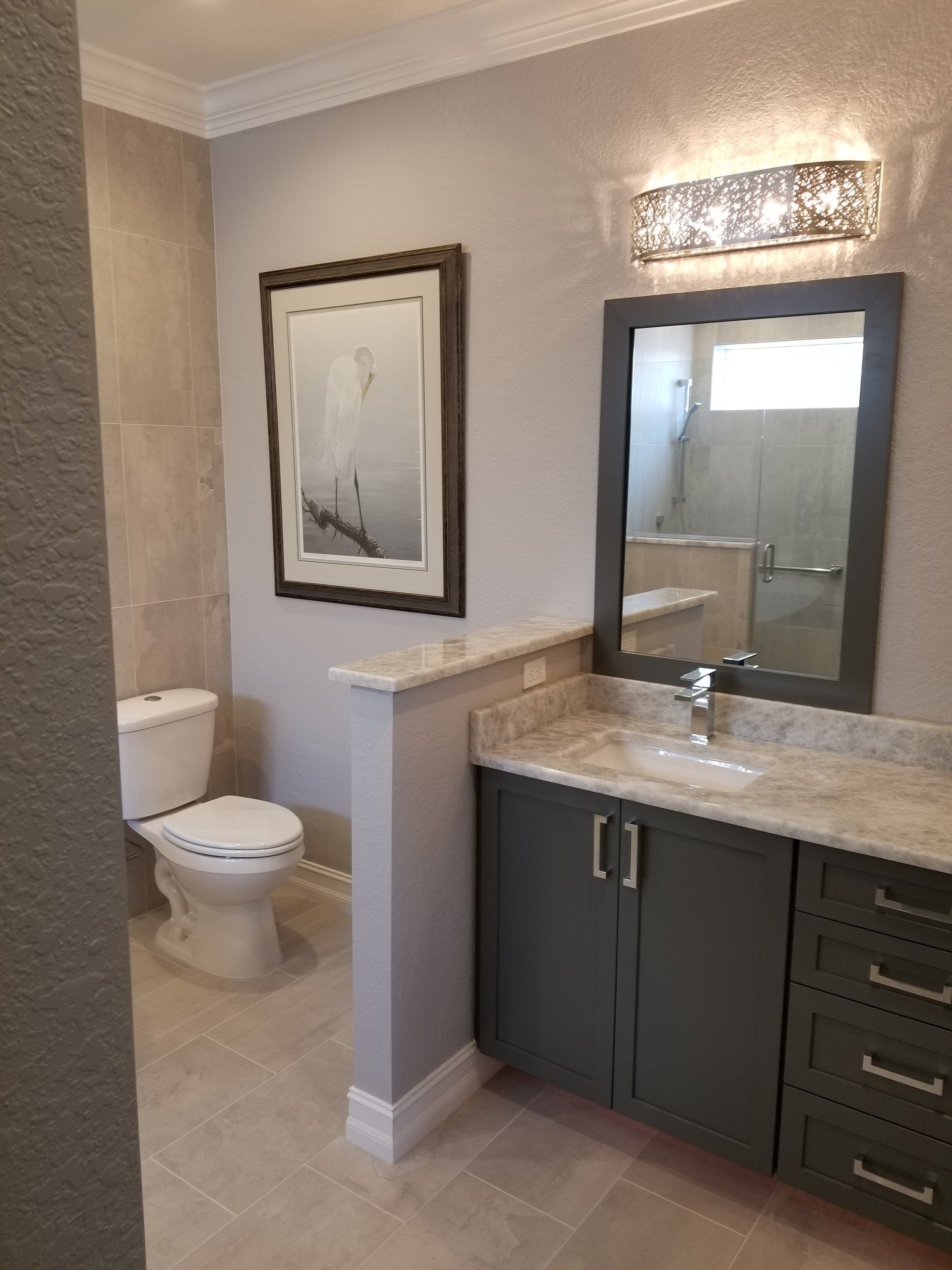 Bathroom with gray vanity, toilet, mirror, and artwork. Light-colored walls and floor.