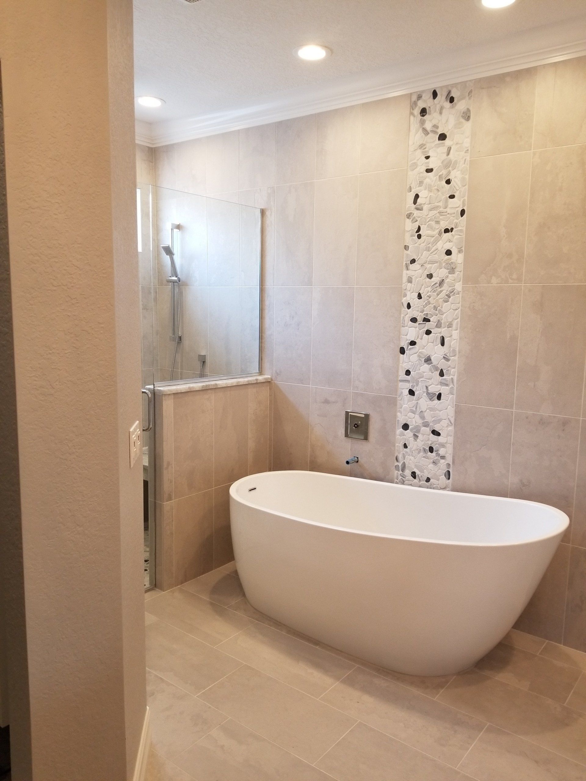 Modern bathroom with a white oval tub, tiled walls, and a glass shower enclosure.