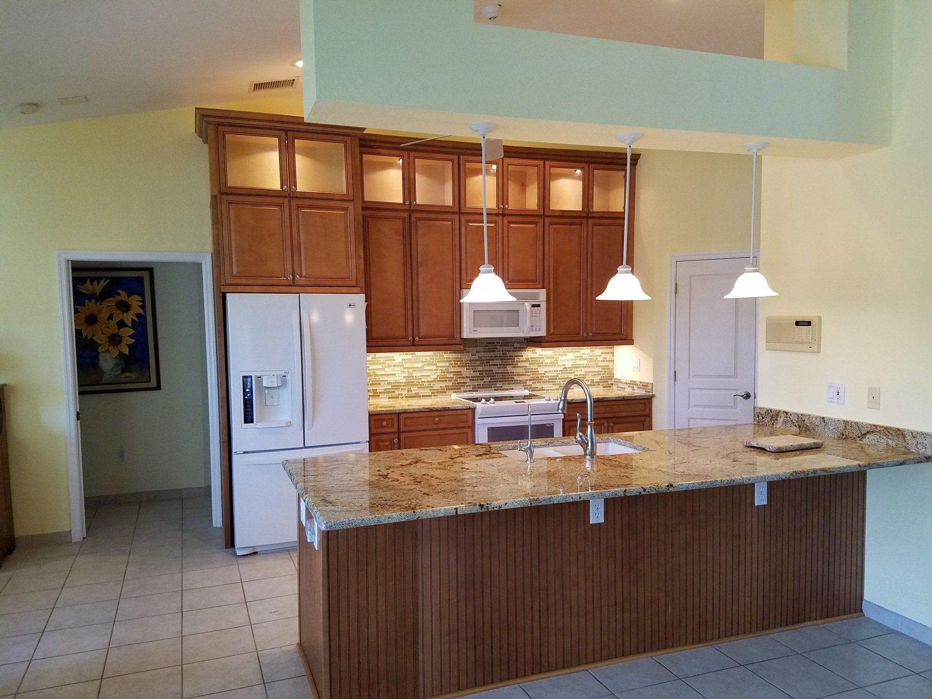 Kitchen with brown cabinets, granite island, white appliances, and pendant lights.