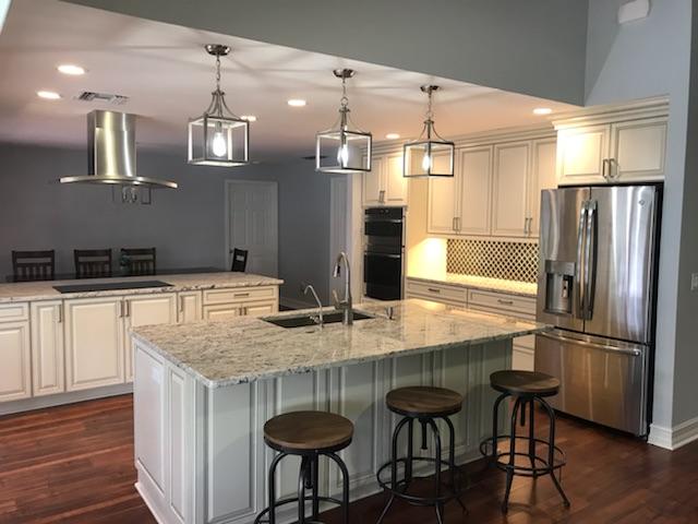 Modern kitchen with white cabinets, granite countertops, island with stools, and pendant lights.