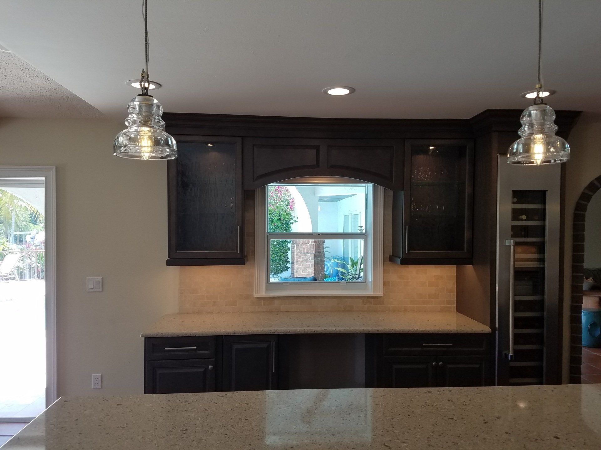 Kitchen with dark cabinets, window, pendant lights, and light countertops.