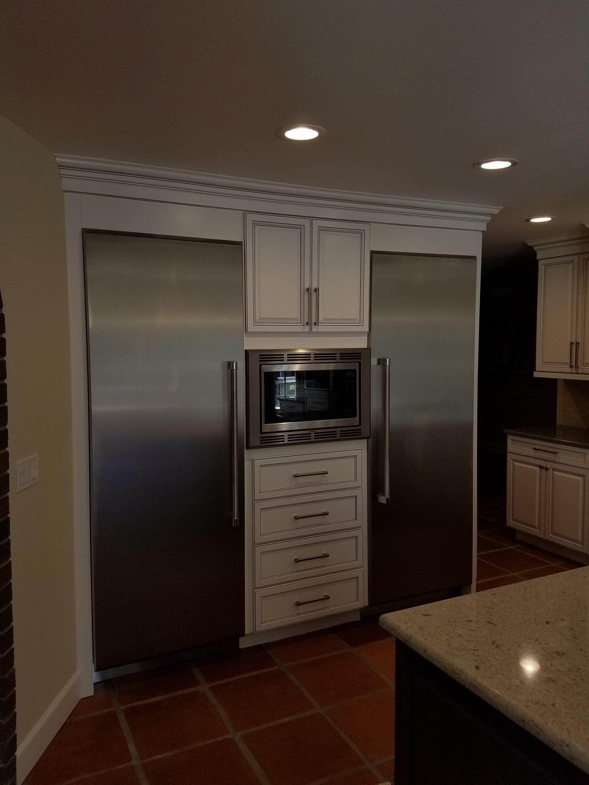 Stainless steel refrigerator and freezer flanking a cabinet with microwave and drawers in a kitchen.