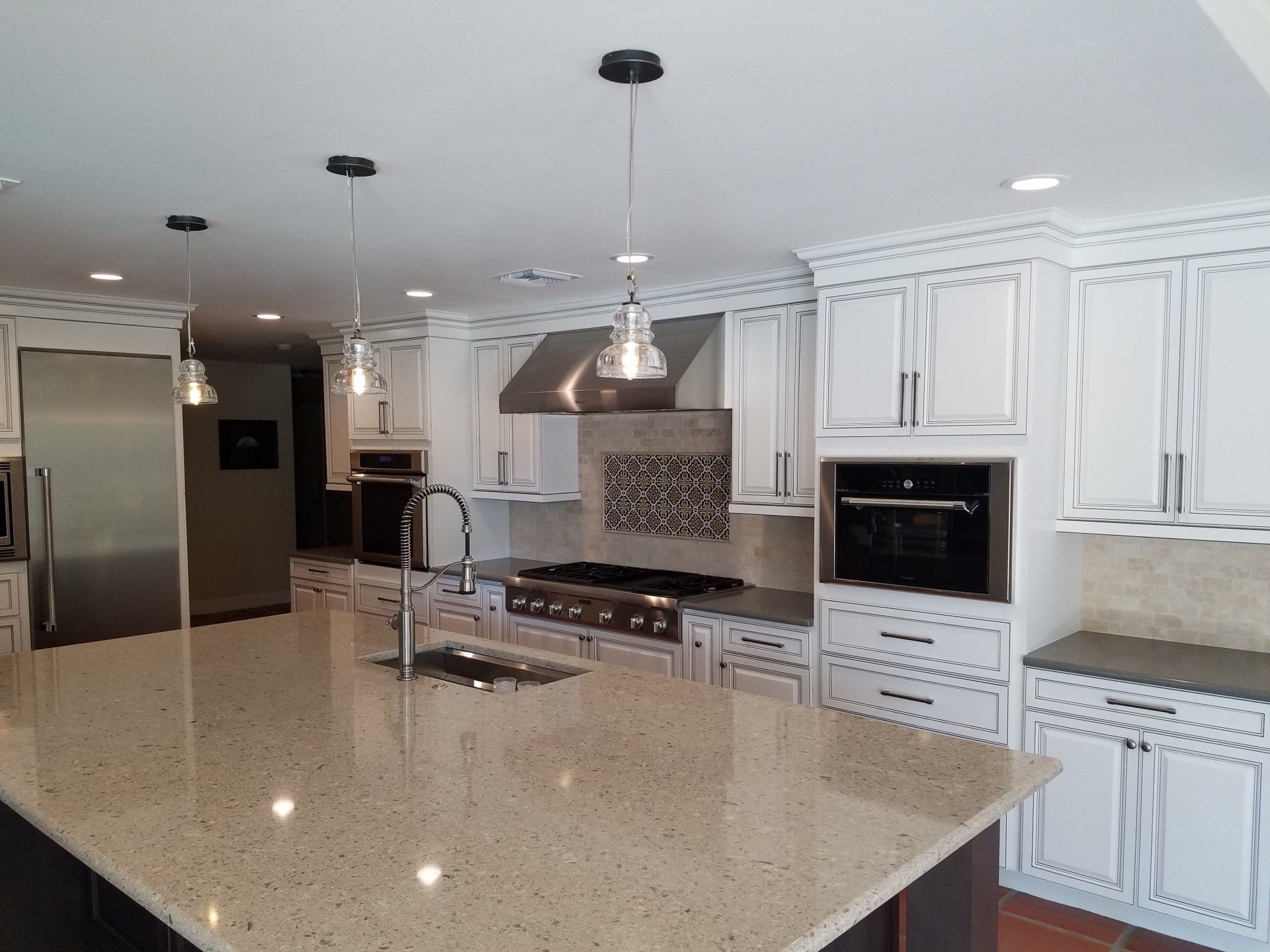Spacious white kitchen with island, stainless steel appliances, and pendant lights.