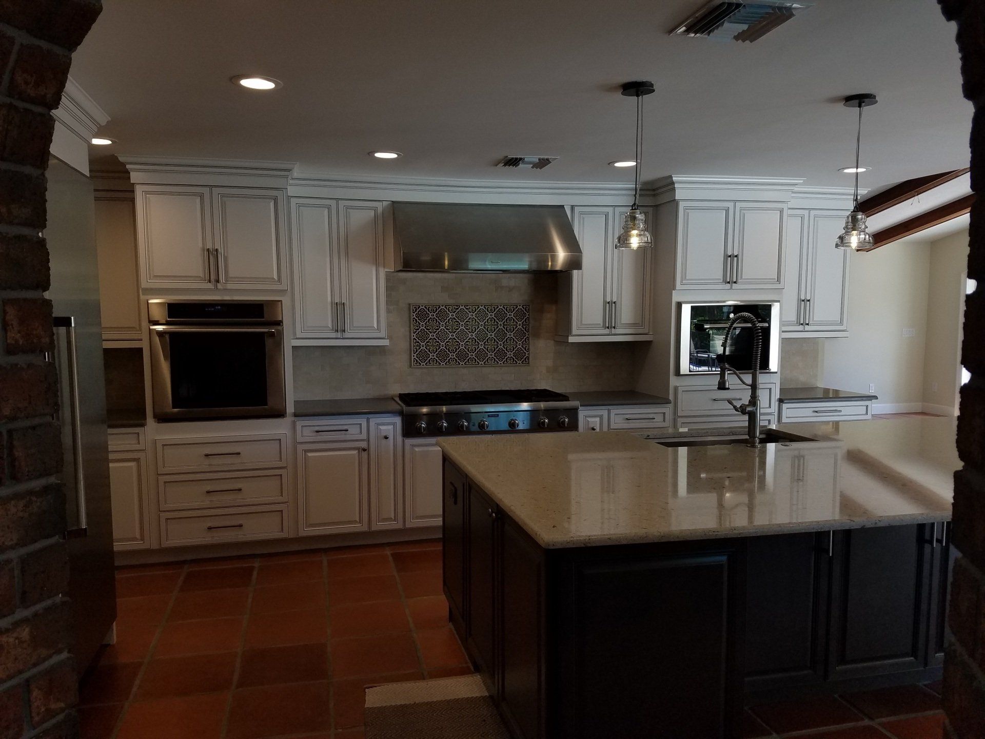 Kitchen with white cabinets, dark island, stainless appliances, and brick archway.