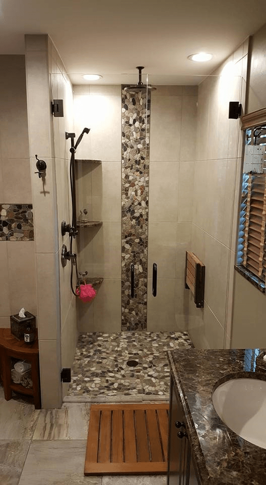 Modern bathroom with glass shower enclosure, pebble floor, and stone tile accent wall.