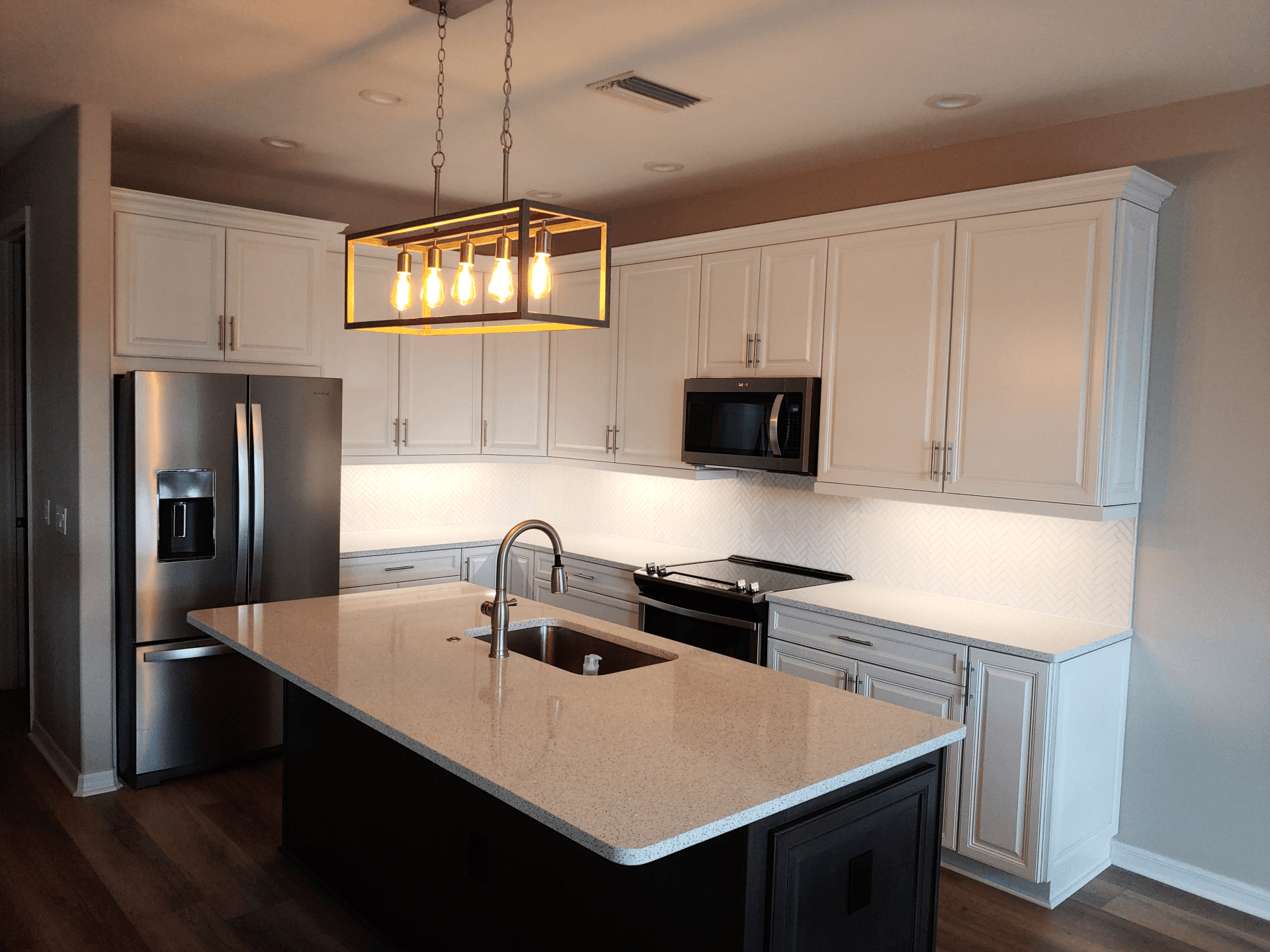 Modern kitchen with white cabinets, stainless steel appliances, dark island, and overhead lighting.