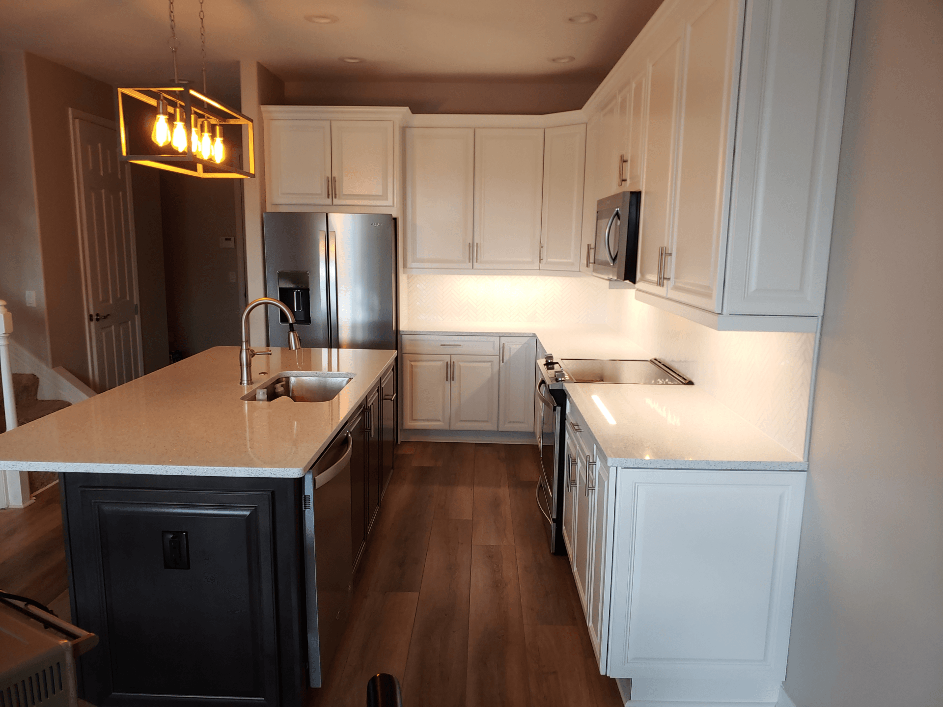 Modern kitchen with white cabinets, dark island, stainless steel appliances, and wood floors.
