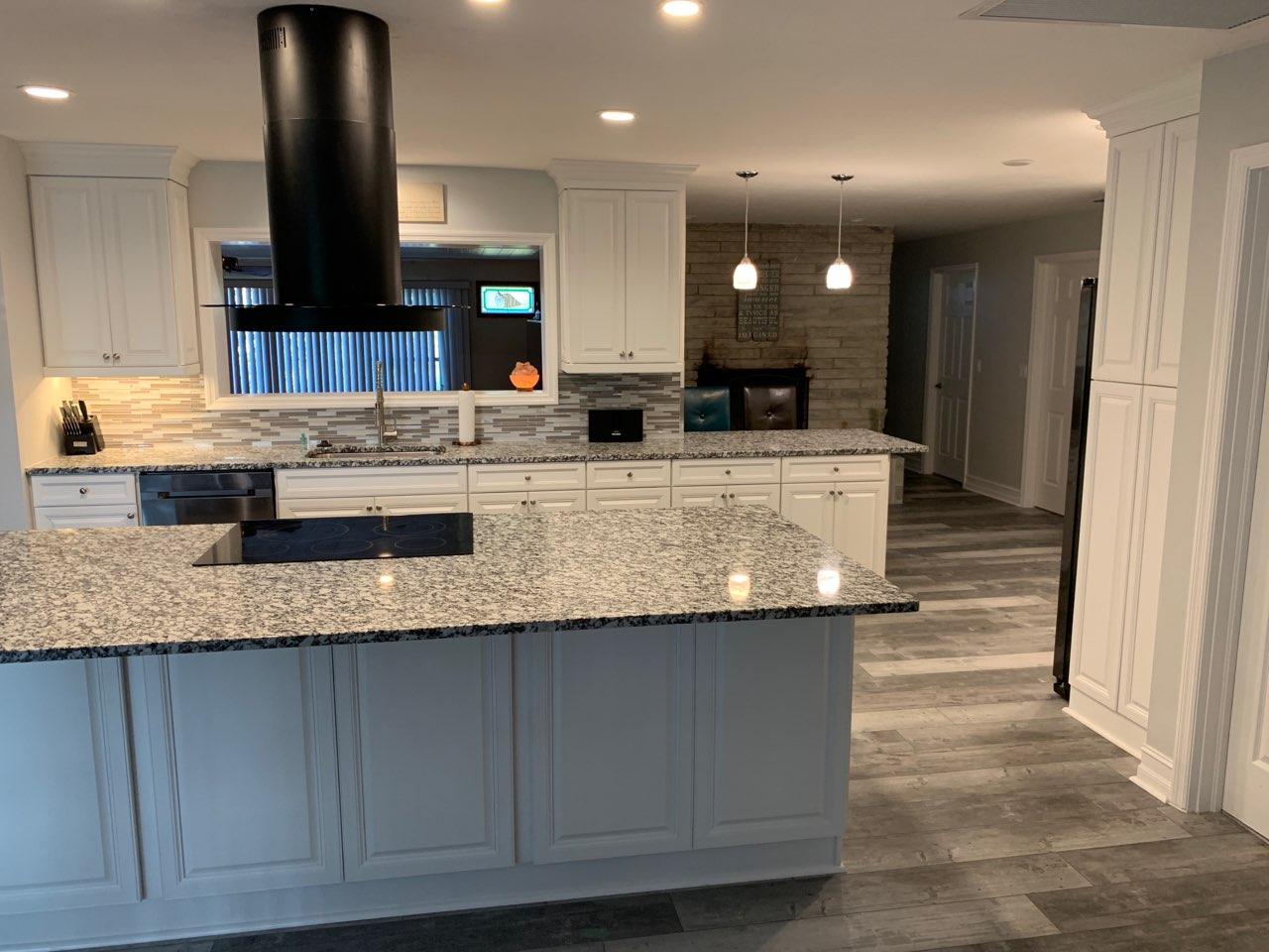 Modern white kitchen with granite countertops, island, black range hood, and hardwood floors.