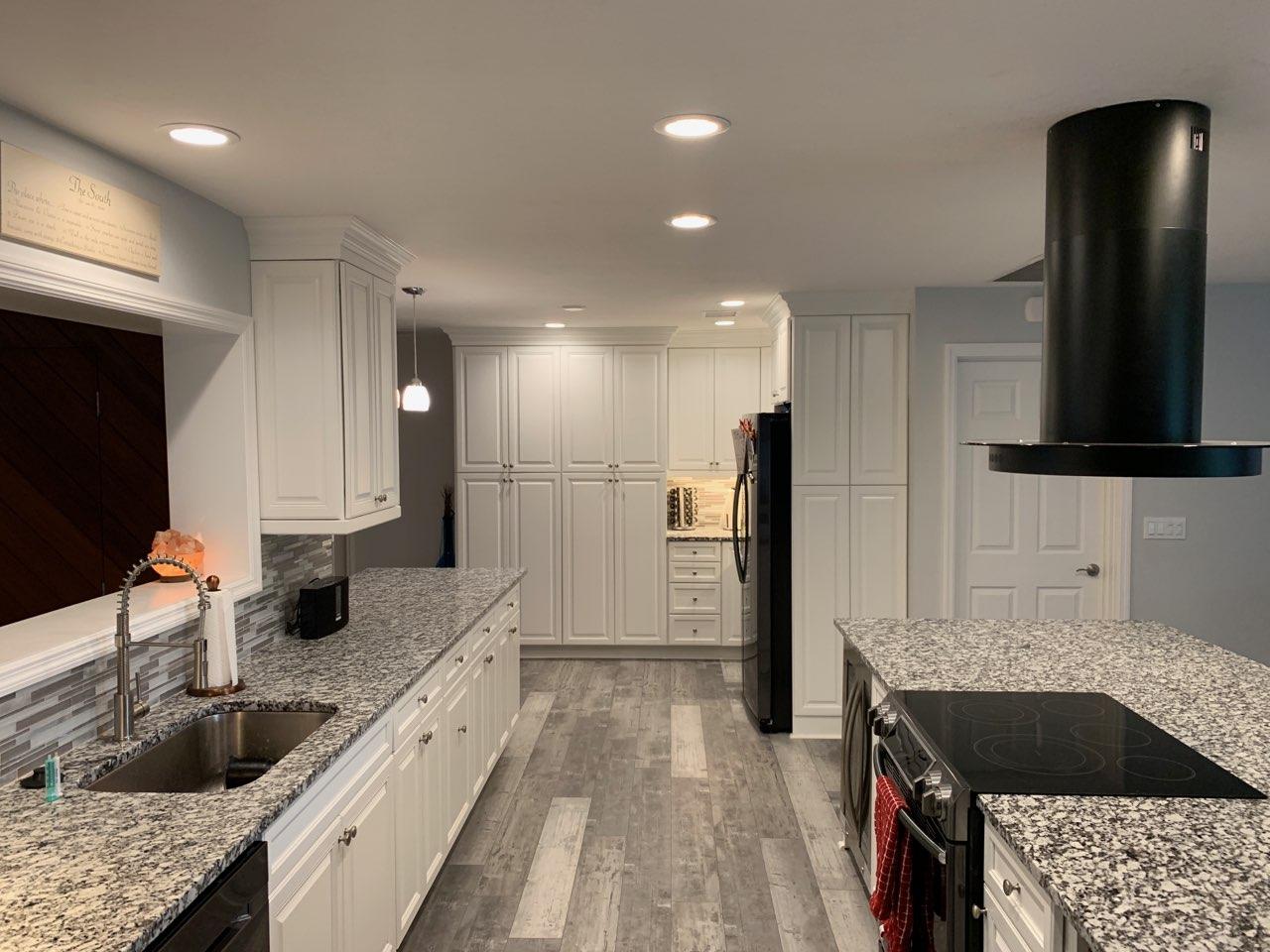 White kitchen with granite countertops, stainless steel appliances, and gray wood-look flooring.