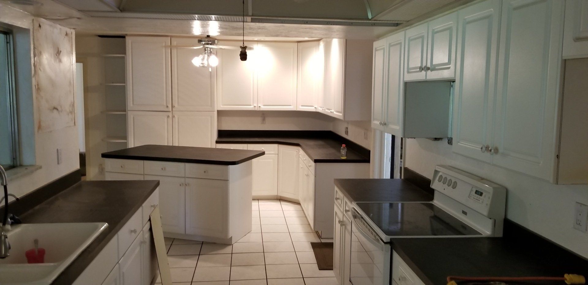 White kitchen with dark countertops, island, and appliances. Fluorescent lighting.