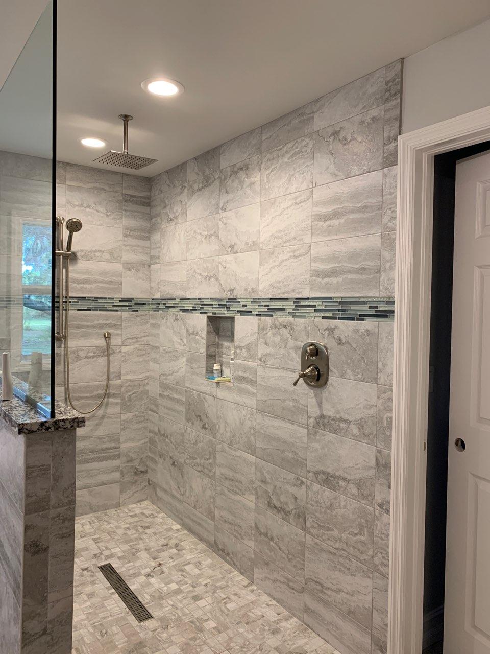 Modern shower with gray tile walls and glass door. Features include a built-in shelf, a showerhead, and a hand shower.