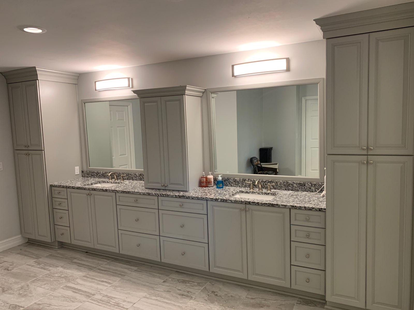 Gray bathroom with double vanity, tall storage cabinets, mirrors, and rectangular light fixtures.