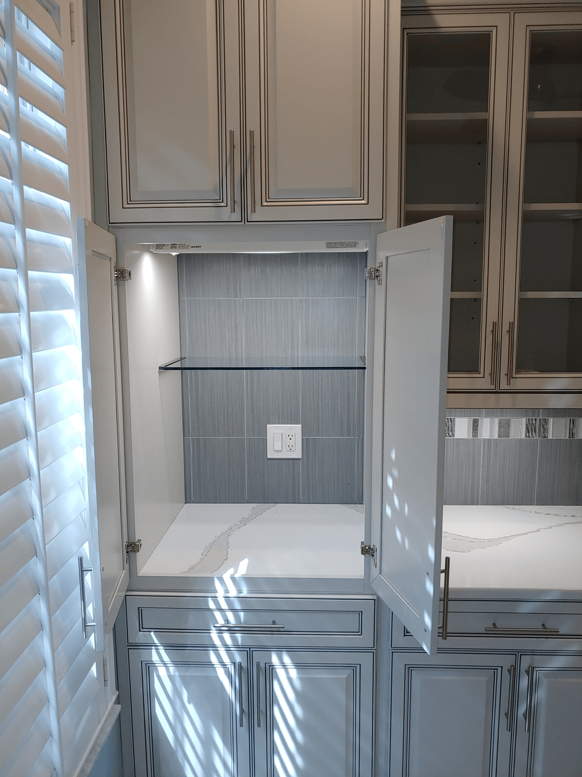 Open cabinet with glass shelf; white cabinets with distressed black trim; power outlet.