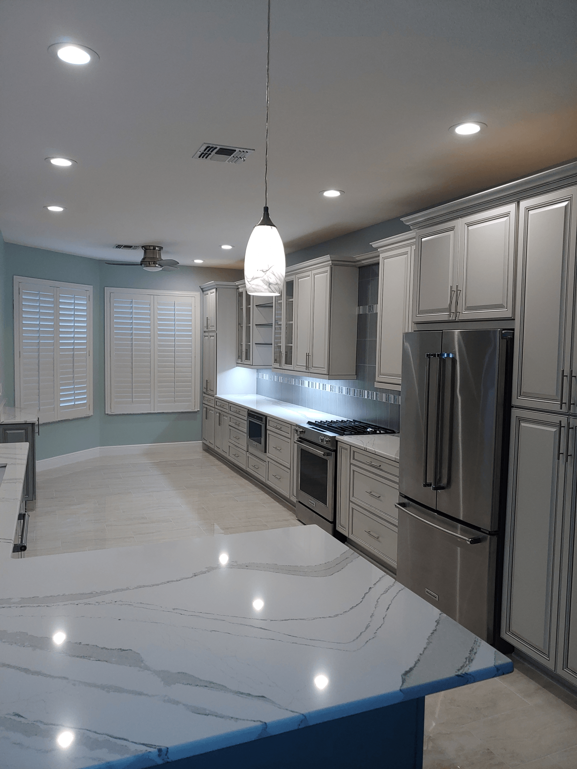 Spacious modern kitchen with light gray cabinets, stainless steel appliances, and white marble countertops.