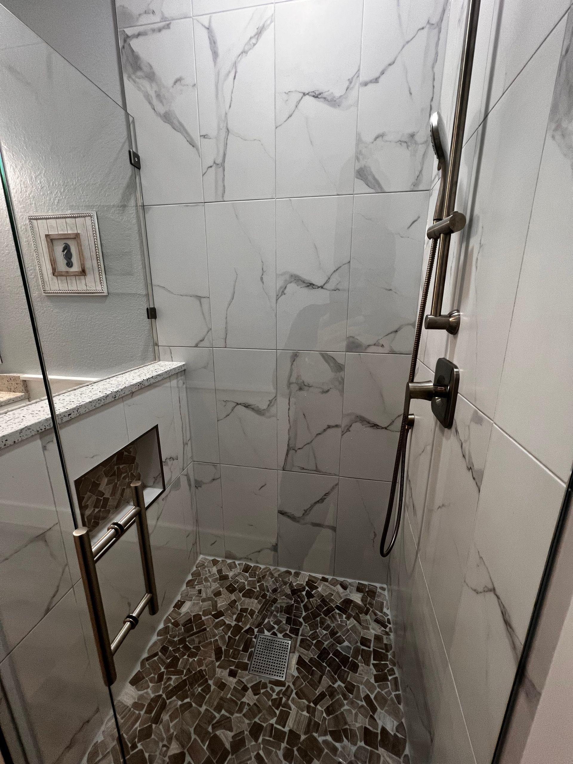 Modern shower with white marble tile, glass door, and a pebble tile seat.