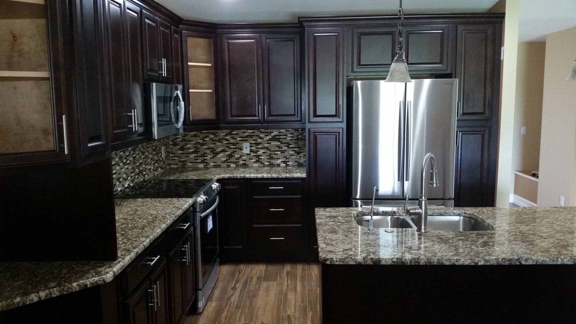 Dark brown kitchen with granite countertops, stainless steel appliances, and hardwood floor.