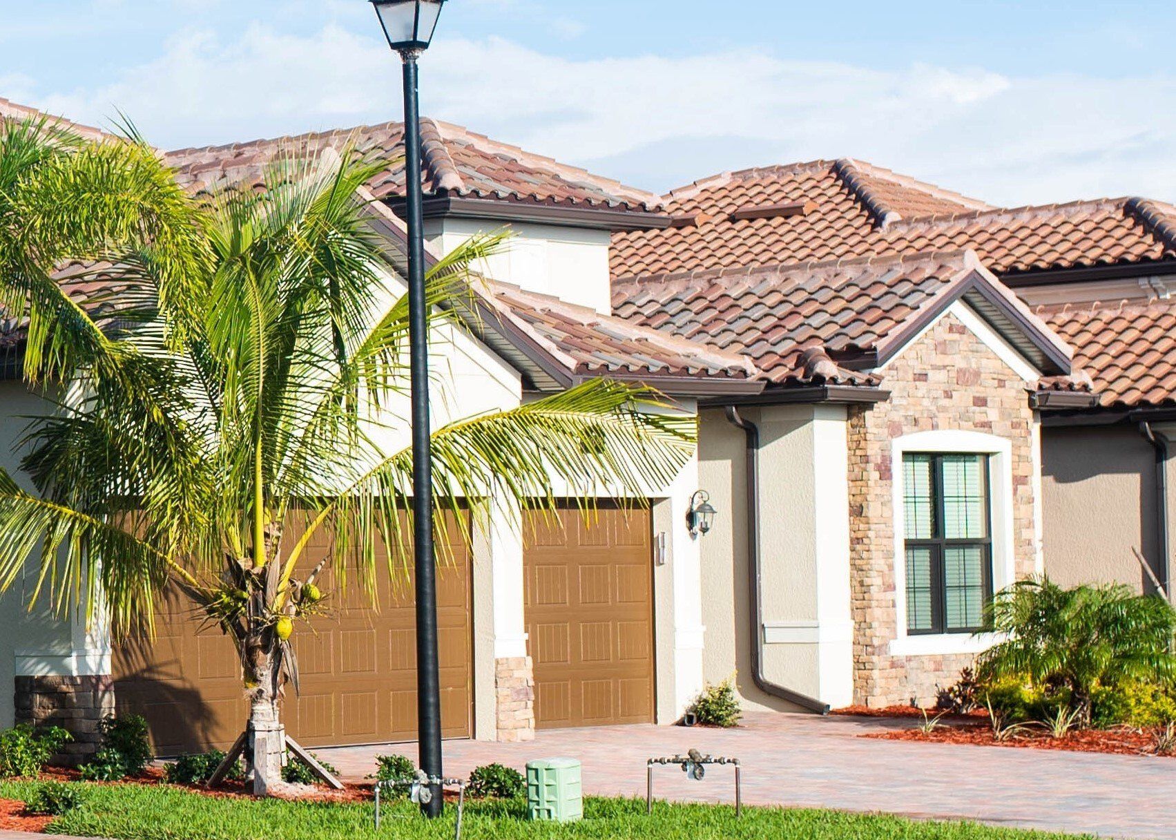 A house with brown garage doors and red tile roof with a palm tree in the front yard.
