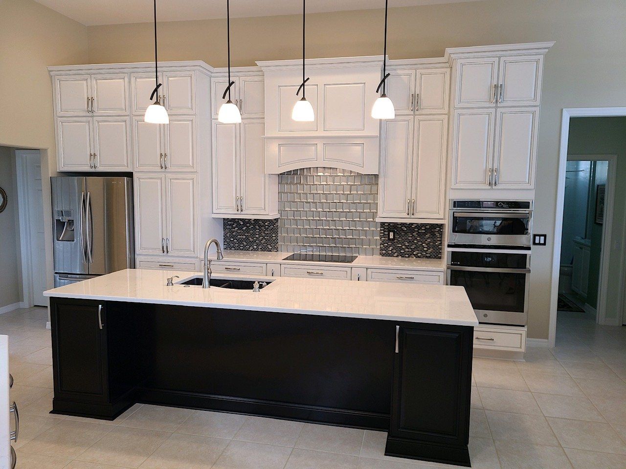 A modern kitchen with white cabinets, black island, stainless steel appliances, and pendant lights.