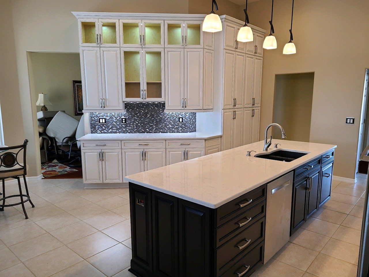 Kitchen with white upper cabinets, dark island with white countertop, and pendant lights.